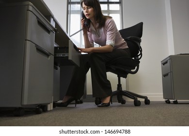 Young businesswoman looking in drawer while talking on telephone in office