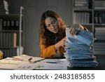Young businesswoman looks stressed while sorting through paperwork at her desk late at night, showing the pressure of the corporate world