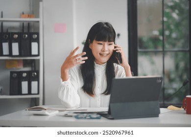 Young businesswoman is multitasking using laptop and talking on phone while working in her office - Powered by Shutterstock