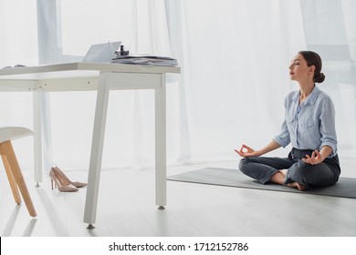 young businesswoman practicing yoga in lotus position with gyan mudra on mat in office - Powered by Shutterstock