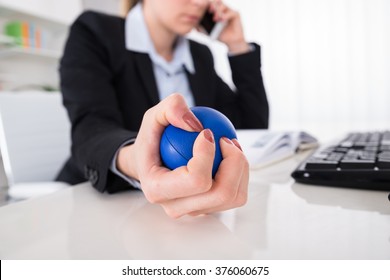 Young Businesswoman Pressing Stressball While Talking On Mobile Phone At Desk