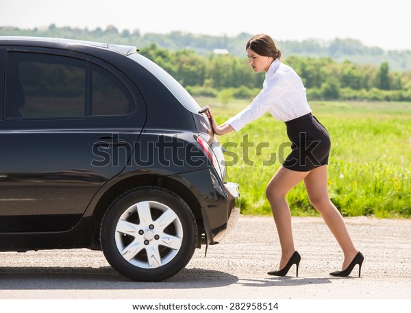 Young\
businesswoman pushing a car with empty fuel\
tank.