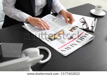 Young businesswoman reading newspaper in office
