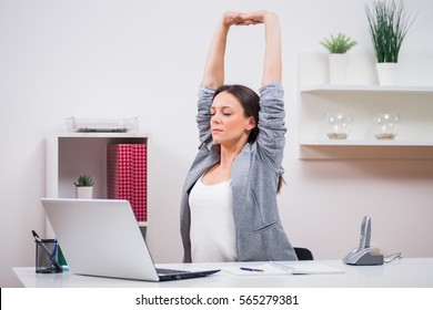 Young businesswoman is relaxing in her office. She is stretching her body. - Shutterstock ID 565279381