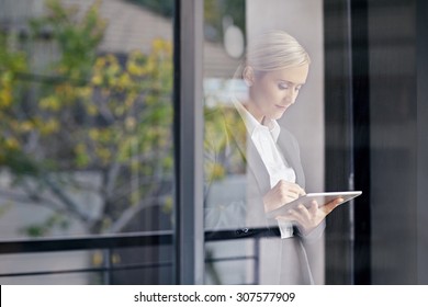 A young businesswoman seen working on tablet through her office window - Powered by Shutterstock