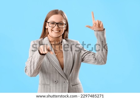 Young businesswoman showing loser gesture and pointing at viewer on blue background