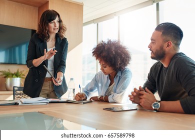 Young Businesswoman Showing Something To Her Colleagues During A Meeting In Conference Room. Multi Ethnic Business Team Discussing Project In Office.