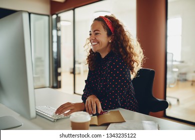 Young businesswoman sitting at her desk and laughing while sitting in a large office working on a computer