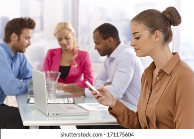 Young businesswoman sitting at a meeting, using mobilephone.