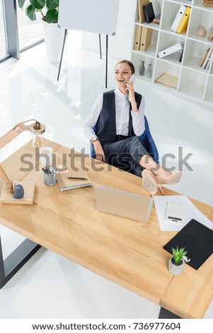 Young businesswoman sitting in office with feet on desk, talking on phone