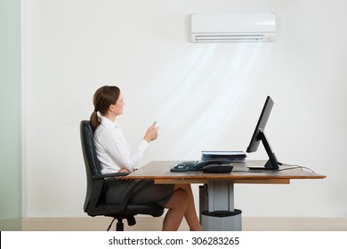 Young Businesswoman Sitting On Chair Using Air Conditioner In Office