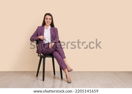 Young businesswoman sitting on chair near beige wall in office, space for text