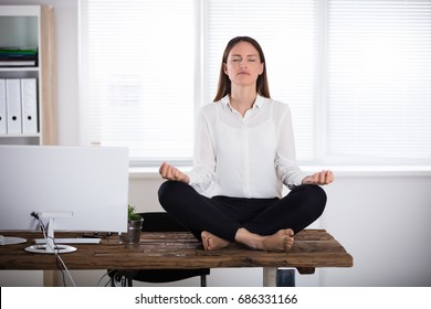 Young Businesswoman Sitting On Wooden Desk Meditating In Office - Powered by Shutterstock