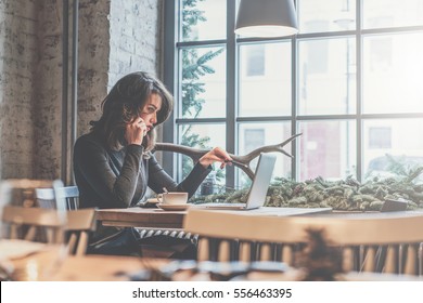 Young Businesswoman Sitting At Table In Cafe And Talking On Mobile Phone. On Table Is Laptop,cup Of Coffee, Notebook. Girl With Pencil Pointing At Computer Screen. Entrepreneur Working Outside Office.