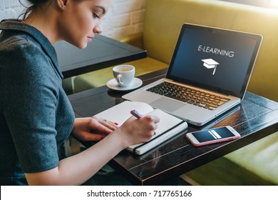 Junge Geschäftsfrau sitzend am Tisch in Café vor Laptop mit Einschreibung auf Bildschirm e-Learning und Bild von quadratischen akademischen Kappe und Noten in Notizbuch, Tagebuch. Online-Bildung, e-Learning.