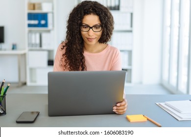 Young businesswoman sitting working at a laptop computer at a table in a modern bright office with copy space