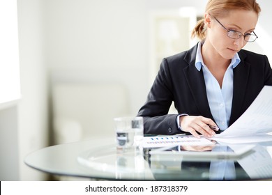 Young businesswoman sitting at workplace and reading paper in office - Powered by Shutterstock