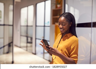 Young Businesswoman Standing In Corridor Of Modern Office Using Mobile Phone - Powered by Shutterstock