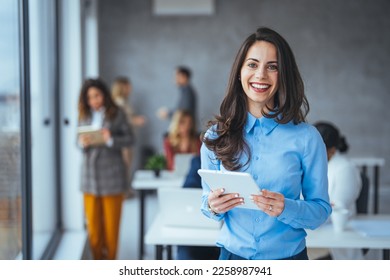 Young businesswoman standing in office with a digital tablet. Confident businesswoman in office. Beautiful businesswoman standing and working on a digital tablet computer in the modern office - Powered by Shutterstock