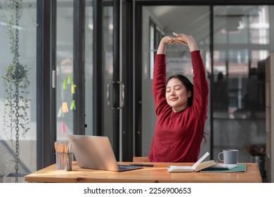 Young businesswoman stretching with hand raised while sitting on a chair in an office. - Powered by Shutterstock