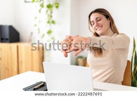 Young businesswoman stretching while working on laptop computer sitting at desk in home office