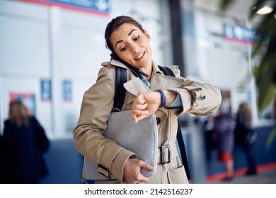 Young businesswoman talking on cell phone and checking the time on her wristwatch while waiting for her transportation at departure area. 