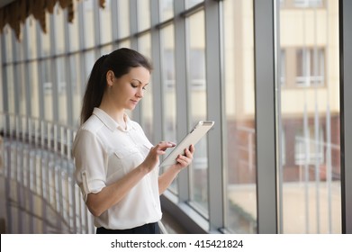 Junge Geschäftsfrau, die sich auf dem Handy unterhält, während sie bei einem Fenster im Büro steht. Schönes junges Frauenmodell im hellen Büro.