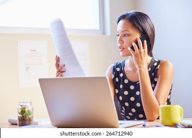A young businesswoman talking on the phone while looking at a document
