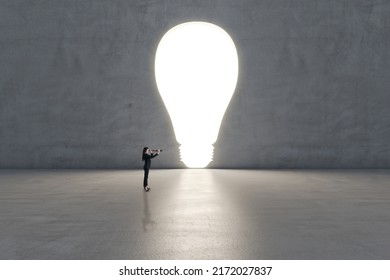 Young businesswoman with telescope standing in concrete interior with bright lamp outline and mock up place on concrete wall. New ideas research, success and strategic planning concept - Powered by Shutterstock