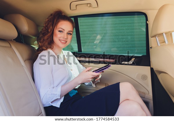 Young businesswoman traveling to\
work in the luxury car on the back seat holding mobile\
phone.
