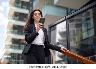 Junge Geschäftsfrau, die ihr Smartphone benutzt, während sie die Treppe in einer modernen Stadt hinuntergeht