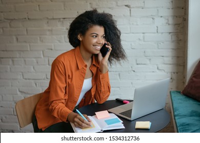 Young businesswoman using laptop, talking on mobile phone, taking notes, planning startup, working from home. Successful business concept. Portrait of beautiful woman freelancer at workplace - Powered by Shutterstock