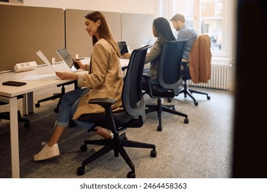 Young businesswoman using laptop while analyzing paperwork while working at co-working office. - Powered by Shutterstock