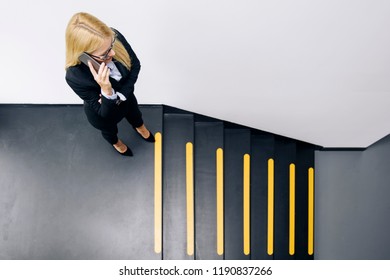 Young businesswoman using mobile phone in office while climbs the stairs - Powered by Shutterstock