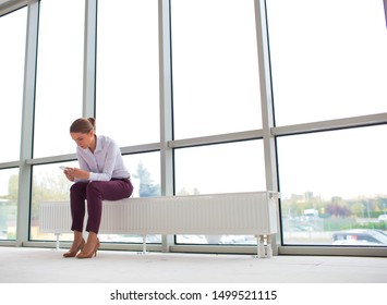 Young businesswoman using smartphone while sitting on radiator at new empty office - Shutterstock ID 1499521115