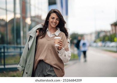 Young businesswoman walks outside her office building, enjoying a cup of coffee on a break, exuding success and professionalism in an urban setting - Powered by Shutterstock