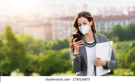 Young Businesswoman Wearing Face Mask Outside During Covid-19 Coronavirus Health Crisis. Professional Woman Using Her Smartphone.