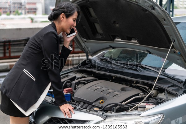 Young businesswoman whose car breakdown uses\
mobile phone to call for roadside assistance service. Travel and\
transportation vehicle\
problem.