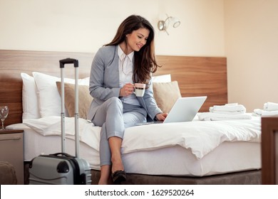 Young Businesswoman Working From Hotel Room On Business Trip, Woman Sitting On Bed And Using Laptop.