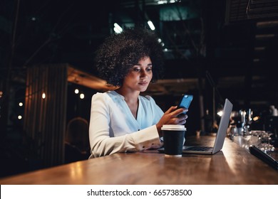 Young Businesswoman Working At Late Night Shift And Using Mobile Phone. African Female Looking At Her Smartphone While Working.