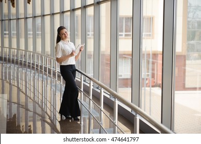 Young Businesswoman Working On Ipad While Standing By Window In Office. Beautiful Young Female Model In Bright Office.