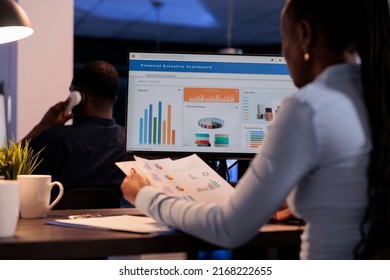 Young businesswoman working with statistics charts on computer monitor, analyzing company data on paperwork. Using online information to create research report before deadline, at night after hours. - Powered by Shutterstock