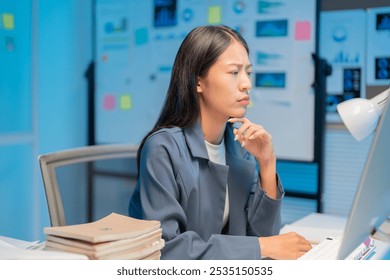 Young businesswoman works late at the office, focused on tasks with a pensive expression, surrounded by paperwork and technology - Powered by Shutterstock