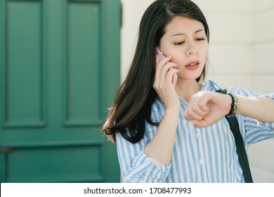 Young Businesswoman Worried Looking At Wrist Watch During Call With Driver. Hurry Office Lady Standing Out Home Door And Waiting To Pick Her Up. Nervous Woman Checking Time Talking On Mobile Phone