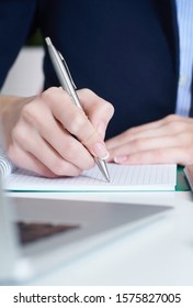 Junge Geschäftsfrau schreibt Notizblock, während sie im Büro sitzt. Weibliche Hände, die einen Stift halten und Notizen in Nahaufnahme machen.
