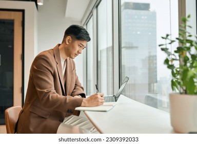 Young busy Asian business man manager working on laptop in office writing notes. Professional businessman analyst using computer checking corporate data, watching online webinar, elearning concept. - Powered by Shutterstock