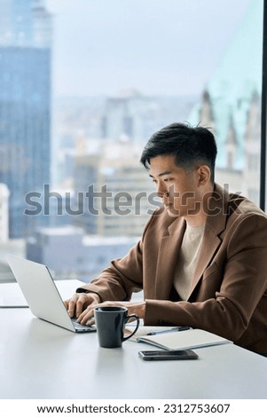 Young busy Asian business man executive working on financial strategy on laptop at corporate office. Professional Japanese businessman manager using computer technology sitting at table, vertical.