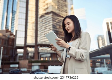 Young busy Asian business woman professional office manager executive standing on big city urban street using digital tablet fintech pad gadget technology connected for work and communication. - Powered by Shutterstock