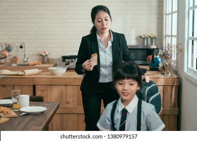 Young Busy Asian Employee Mother Rushing With Daughter In Morning Going Faster Late For Work And School. Mom Businesswoman Take Away Toast Breakfast Hold Backpack. Child In Uniform Smiling Walk Leave