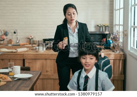 young busy asian employee mother rushing with daughter in morning going faster late for work and school. mom businesswoman take away toast breakfast hold backpack. child in uniform smiling walk leave